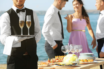 Waiter with champagne at buffet catering party outdoors near river