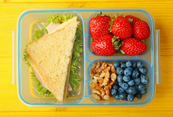 Sandwich and berries in lunchbox on yellow wooden background