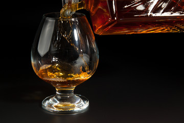 Cognac is poured from a bottle into  glass