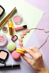 Fototapeta premium Woman holding macaron cookie over makeup products