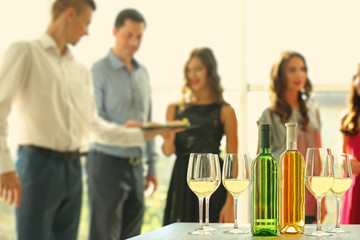 Bottles and glasses of white wine on table against blurred party background