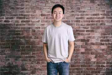 Asian man in blank grey t-shirt standing against brick wall