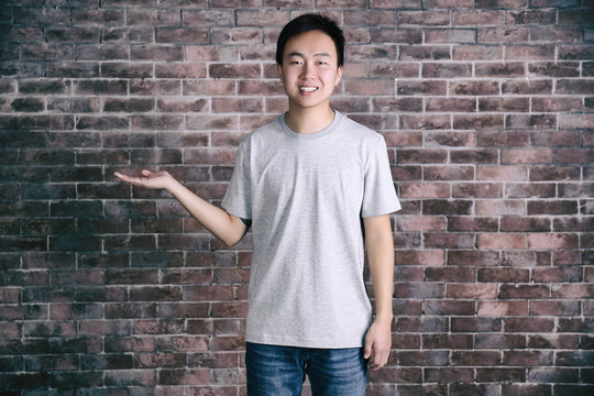 Asian man in blank grey t-shirt standing against brick wall