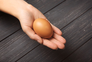 Female hand with egg on wooden background, closeup