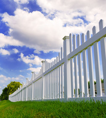 Contemporary white vinyl fence spanning across a homes backyard with grass and blue sky and clouds...