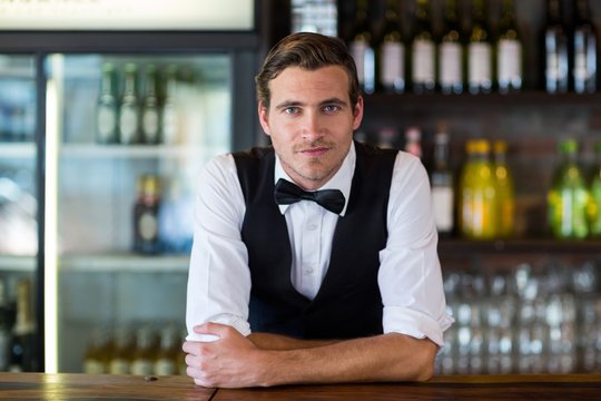 Portrait of bartender leaning on bar counter