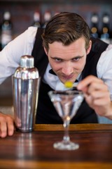Bartender garnishing cocktail with olive
