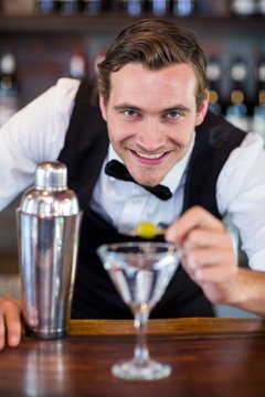 Portrait of bartender garnishing cocktail with olive