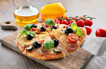 Sliced tasty pizza and fresh cherry tomatoes on wooden cutting board