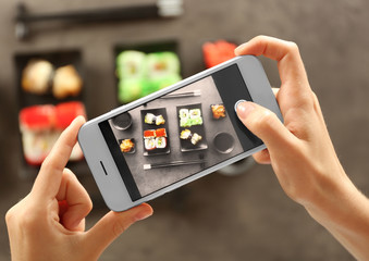 Woman taking photo of tasty sushi set