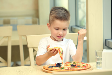 Cute boy eating pizza in restaurant