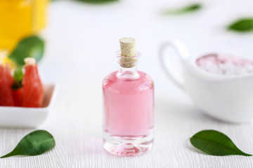 Bottle with essential oil and leaves on wooden table