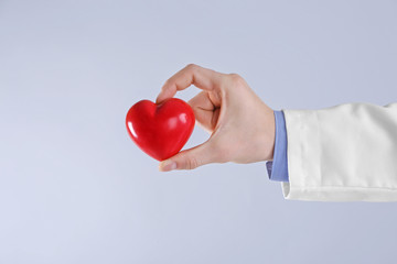 Male doctor hand holding red heart on light background, close up view