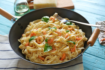 Pan with tasty alfredo pasta, fork and napkin on wooden table