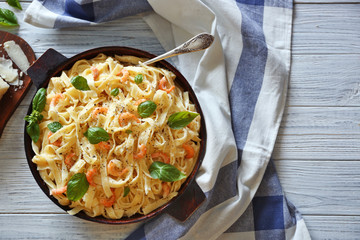 Pan with tasty alfredo pasta, napkin and fork on wooden table, top view
