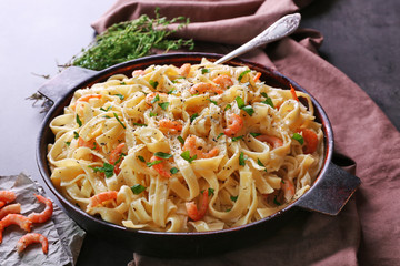 Pan with tasty alfredo pasta, napkin, prawns and herbs on dark table