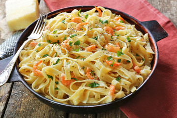 Pan with tasty alfredo pasta, red napkin, grater, cheese and fork  on wooden table