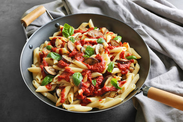 Pan with macaroni, basil, ketchup, eggplant slices and napkin on dark table