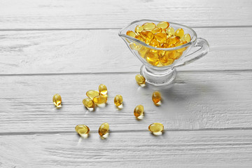 Glass bowl with cod liver oil pills on white wooden table