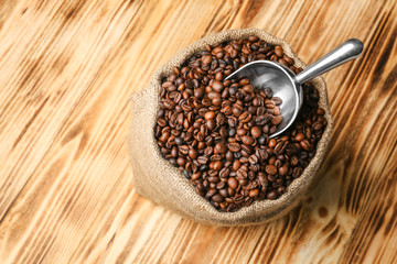 Sack with coffee beans and scoop on wooden background