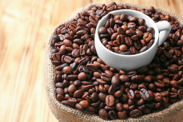 Sack with roasted coffee beans and white cup, close up view