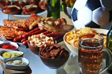 Ball, beer and tasty snacks on kitchen table, close up view
