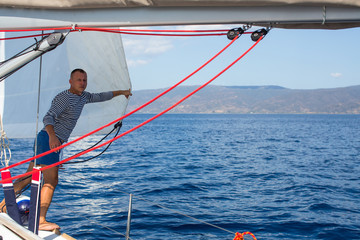 Young man near the sails on the boat. Setting the equipment on a sailing ship during sea yacht race.