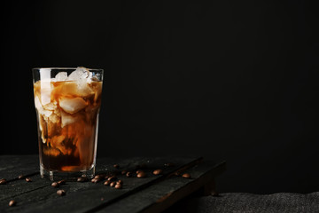 Pouring cream into a glass with iced coffee on table and black background