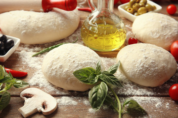 Raw pizza dough with ingredients on wooden table