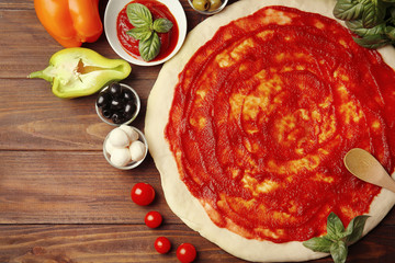 Raw pizza dough with sauce and ingredients on wooden table