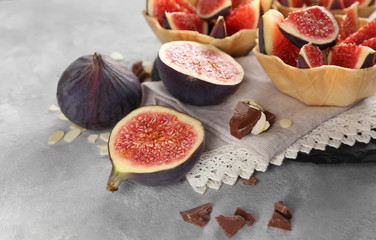 Tasty baskets with fresh figs on napkin on light background