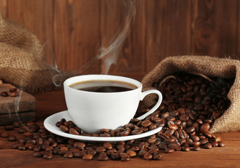 Cup of fresh coffee and sack with beans, closeup