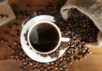 Cup of fresh coffee and sack with beans on wooden background, top view