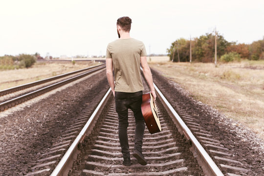 Handsome man with guitar on railroad