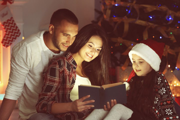 Little girl and her family reading book in living room decorated for Christmas