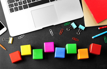 Laptop, copybook and wooden cubes on color background