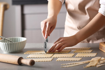 Fototapeta na wymiar Woman cutting dough for ravioli on table