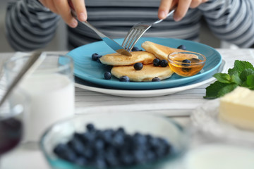 Woman eating tasty pancakes with blueberry on kitchen