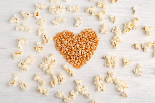 Heart made of corn grains with popcorn on white wooden table