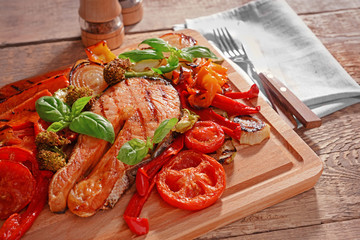 Grilled vegetables with slice of red fish on wooden cutting board