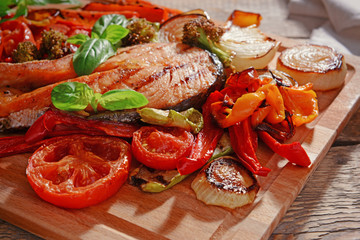 Grilled vegetables with slice of red fish on wooden cutting board, closeup