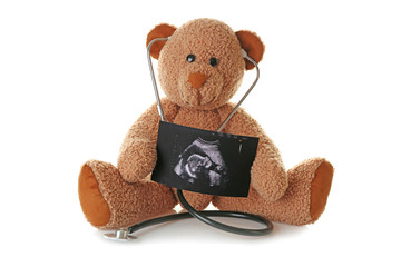 Teddy bear with ultrasound scan of baby and stethoscope on white background