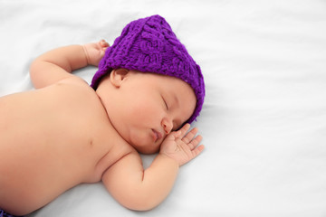 Cute baby in purple hat sleeping on bed