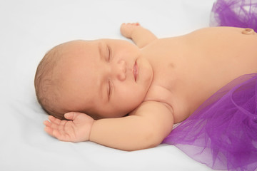 Cute baby in purple skirt sleeping on bed