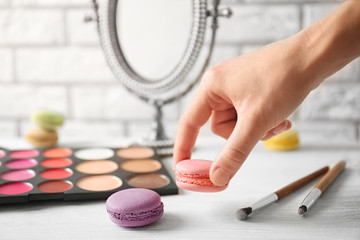 Woman holding macaroon above beauty accessories on table