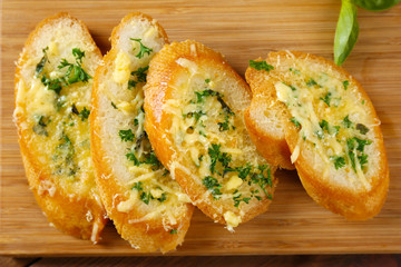 Tasty bread with garlic, cheese and herbs on wooden kitchen board, close up