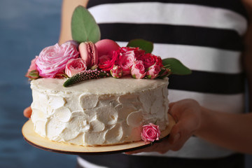 Female hands holding delicious creamy cake with flowers and macaroons closeup