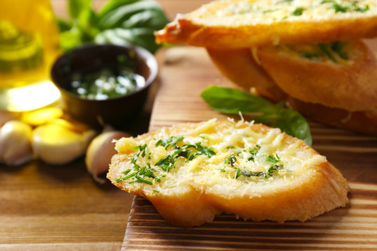 Tasty bread with garlic, cheese and herbs on wooden kitchen board, close up