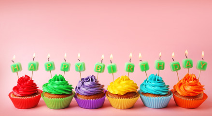 Birthday cupcakes with candles on color background