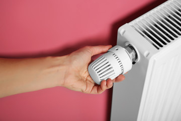 Female hand on temperature regulator of heating battery on pink background, closeup